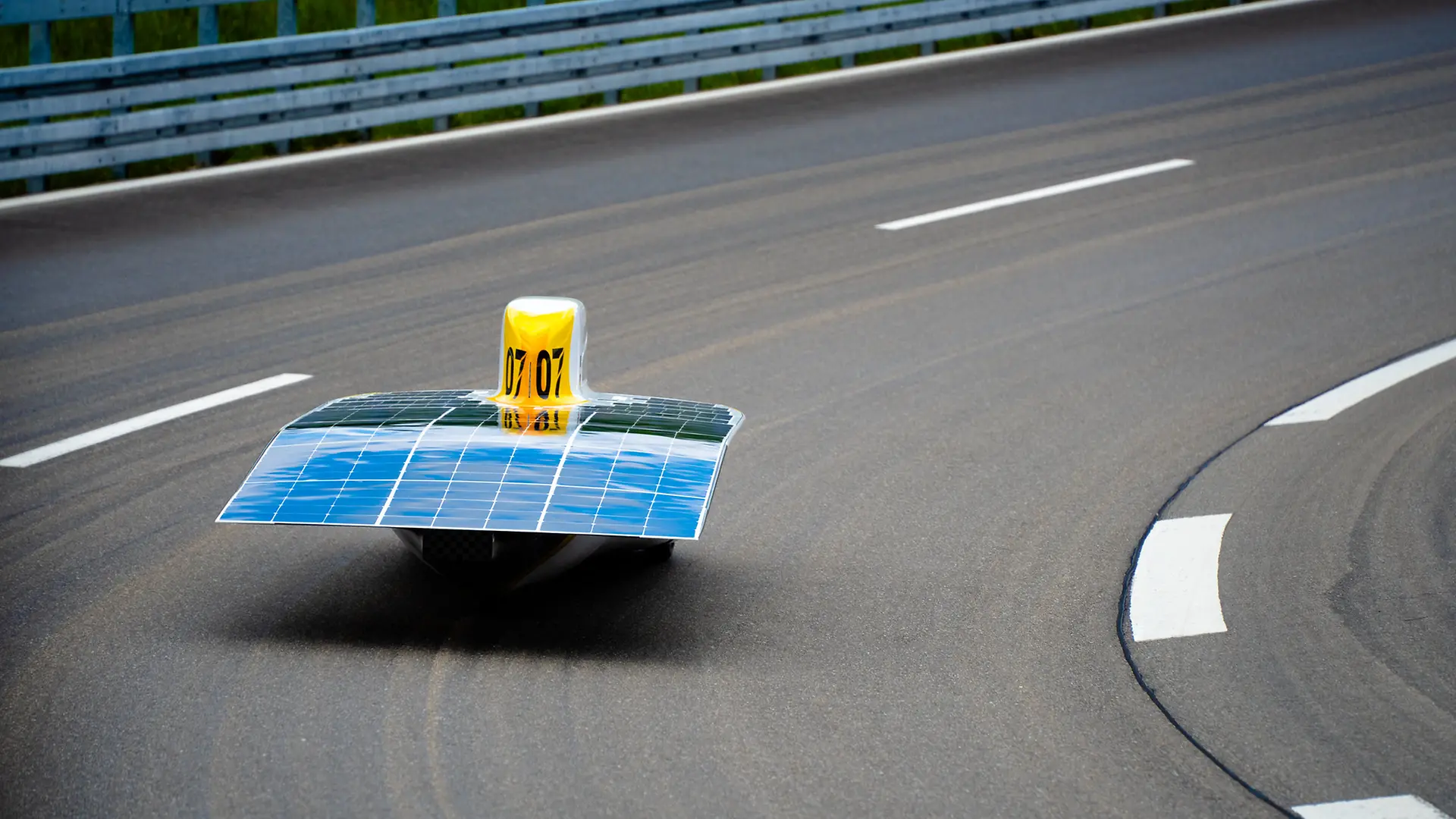 The Sonnenwagen is seen from behind as it drives on an asphalt road. The solar deck with blue solar panels is clearly visible. 