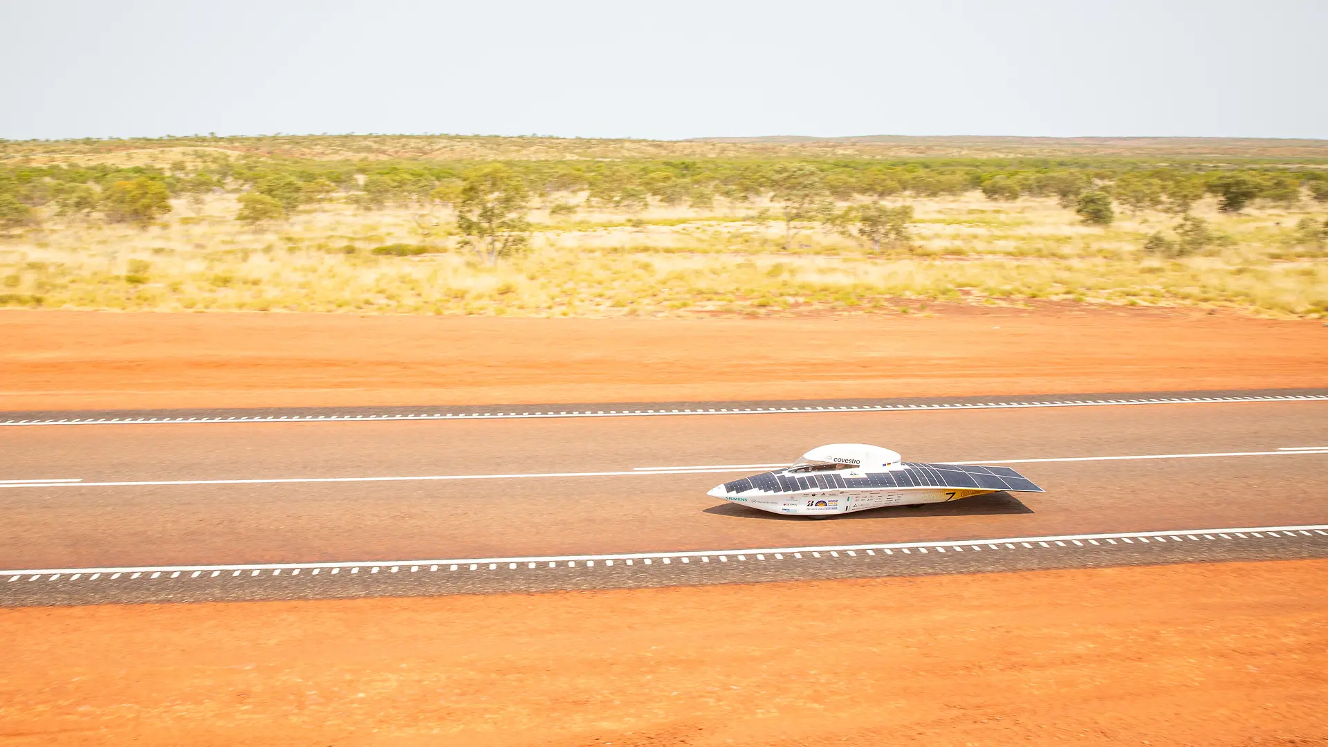 The Sonnenwagen is driving on a road through a desert-like landscape with dry grass and sparse vegetation.