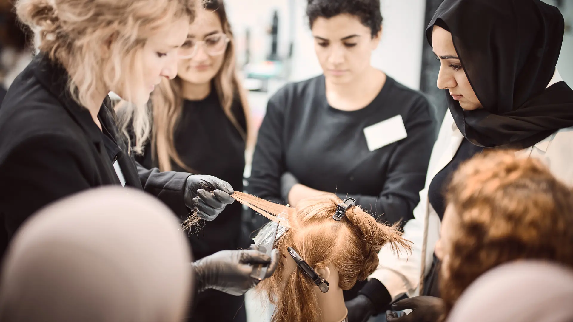 A Shaping Futures trainer demonstrates hair coloring techniques to participants using a mannequin head.