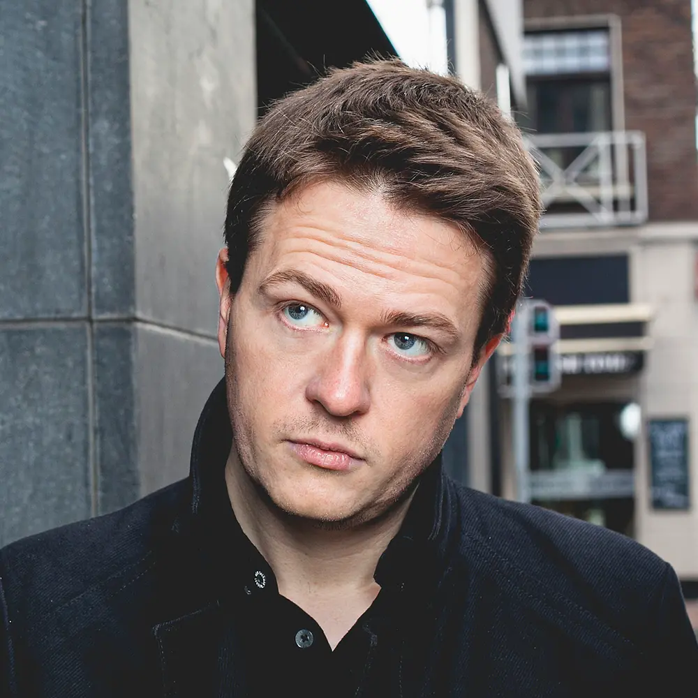 Johann Hari, a British journalist and author of “Stolen Focus” is standing outdoors near a building.